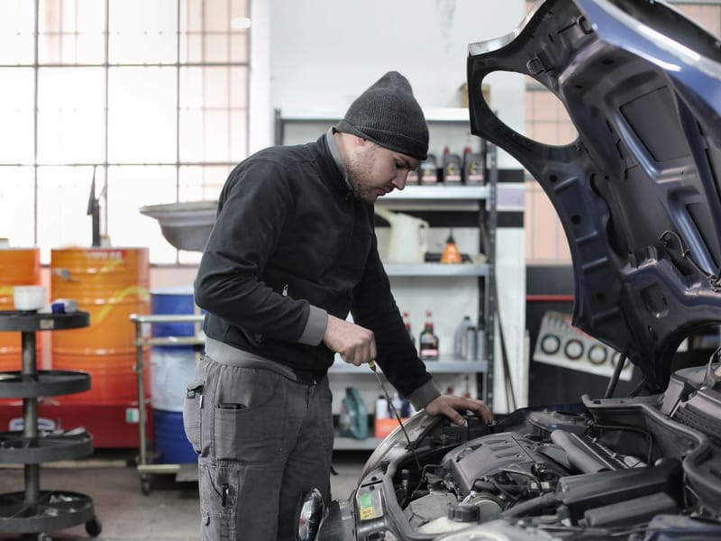 Mechanic checking a car engine under an open bonnet in a repair workshop