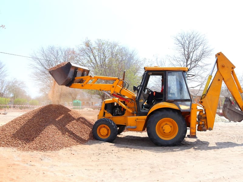 Backhoe loader tipping gravel from its front bucket at a work site