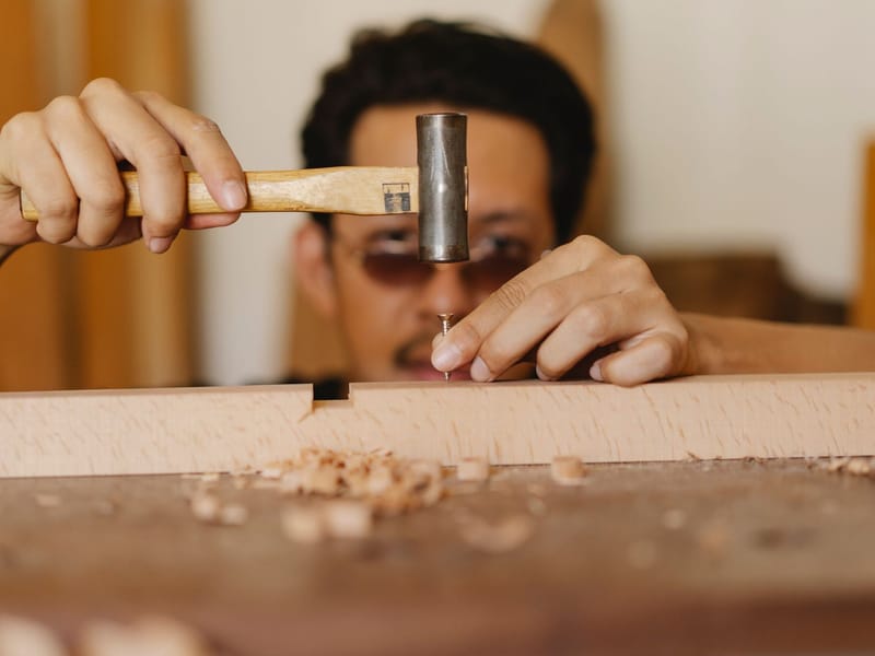 Carpenter hammering a nail into a wooden beam in a workshop