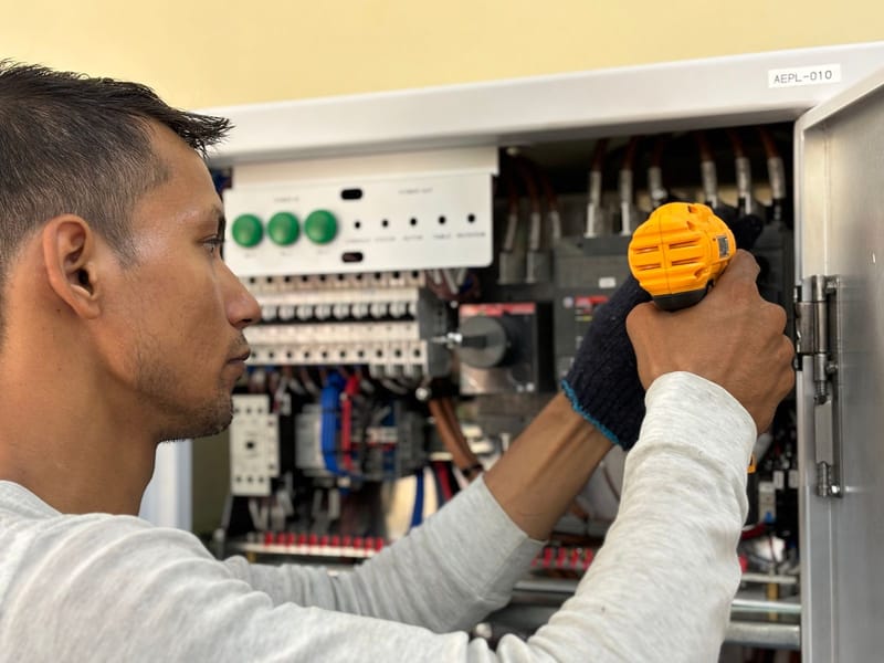 Electrician using a power drill on an electrical control panel