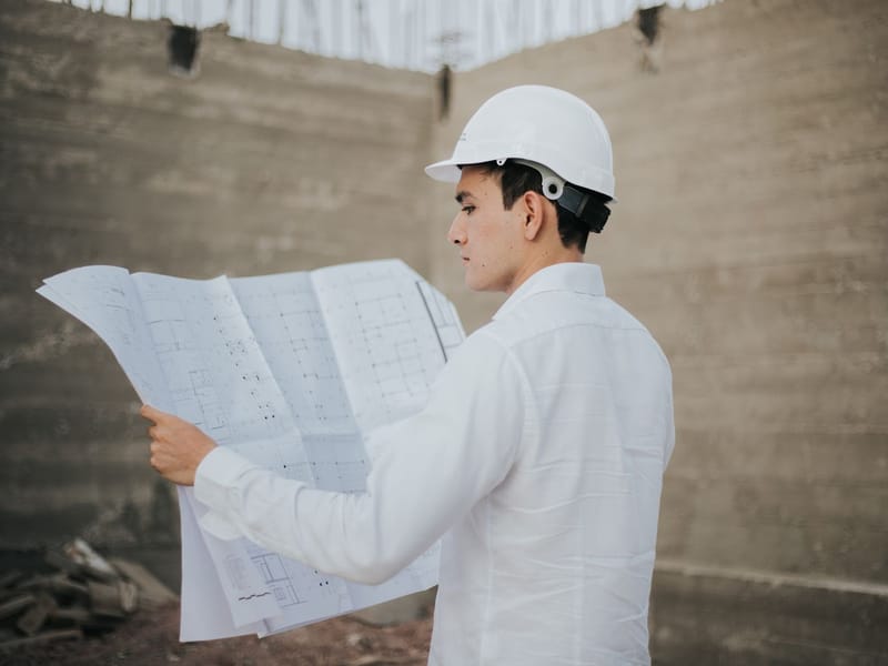 Engineer in a white hard hat reviewing building plans on a construction site