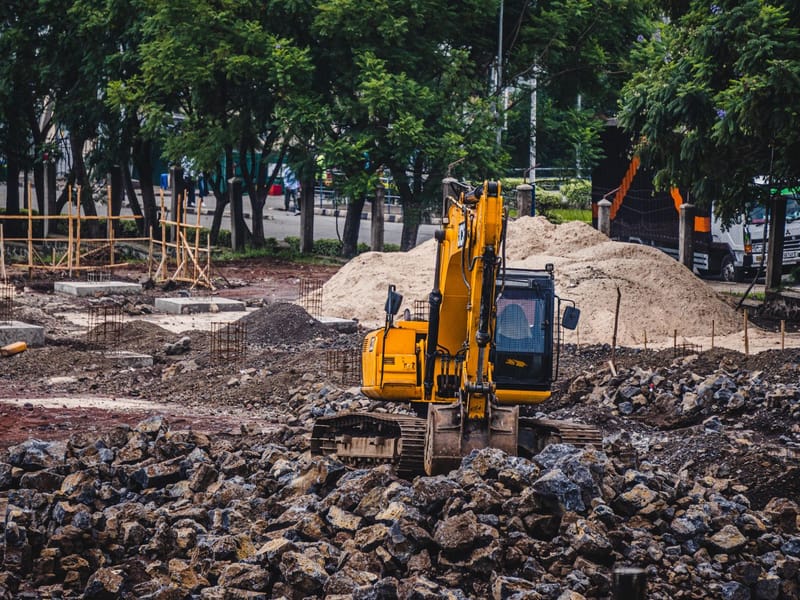 Yellow tracked excavator working on a construction site among rocks and sand piles
