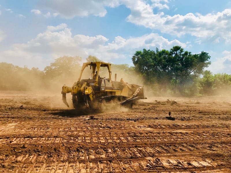 Bulldozer clearing land on a dusty site under a cloudy sky