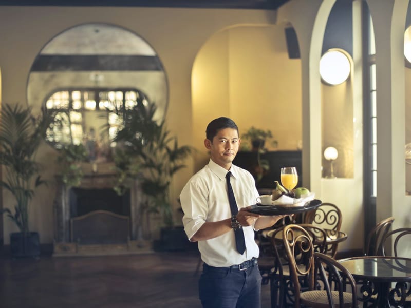 Waiter in shirt and tie carrying a breakfast tray in a restaurant