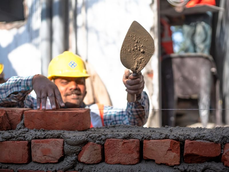 Mason in a hard hat laying bricks with a trowel on a construction site