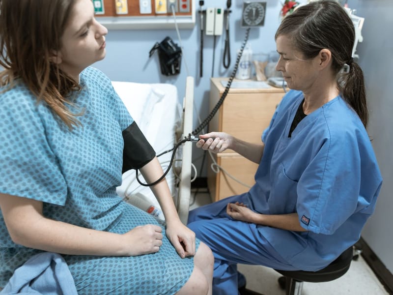 Nurse in blue scrubs checking a patient's blood pressure in a hospital room