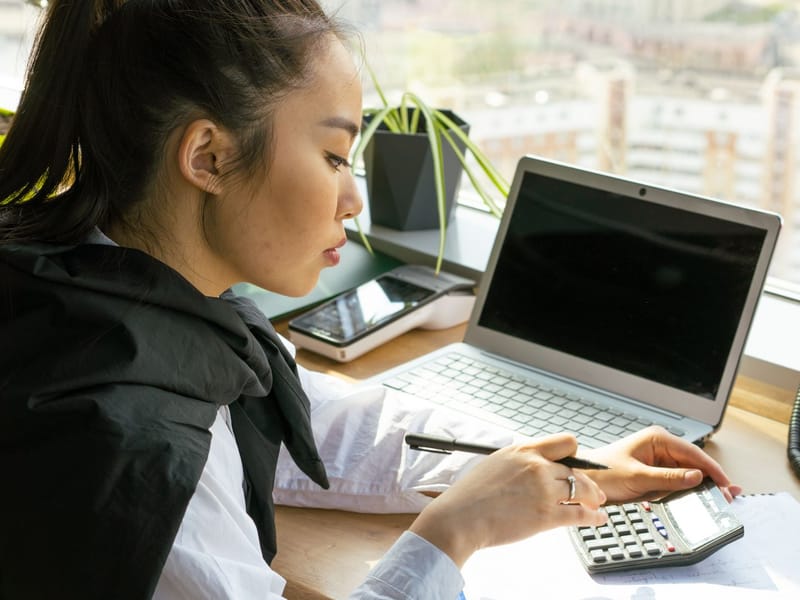 Office worker using a calculator beside a laptop at a desk