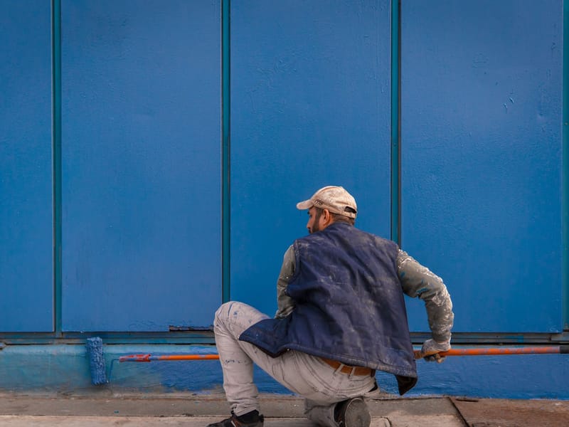 Painter using a long-handled roller on a blue wall