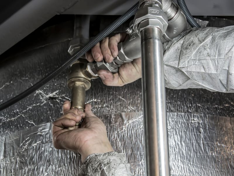 Plumber's hands tightening a valve on metal water pipes