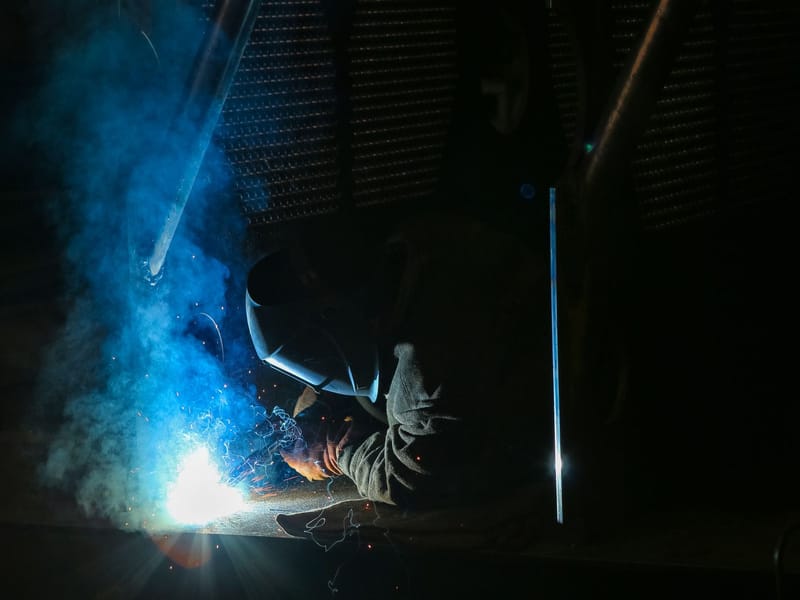 Welder in a protective mask welding metal with bright sparks and smoke
